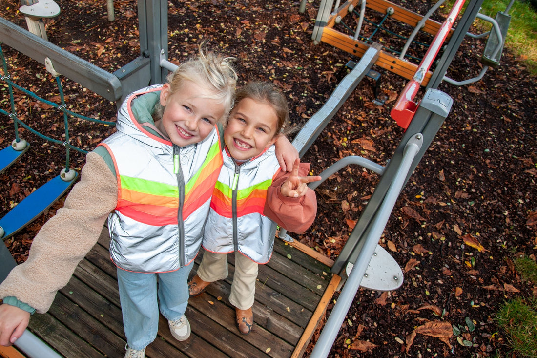 Twee lachende kinderen in een reflecterend Darkflow Kids-hesje met fluo regenboogkleuren